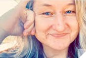 A person with blue eyes and hand on her head

Description automatically generated
